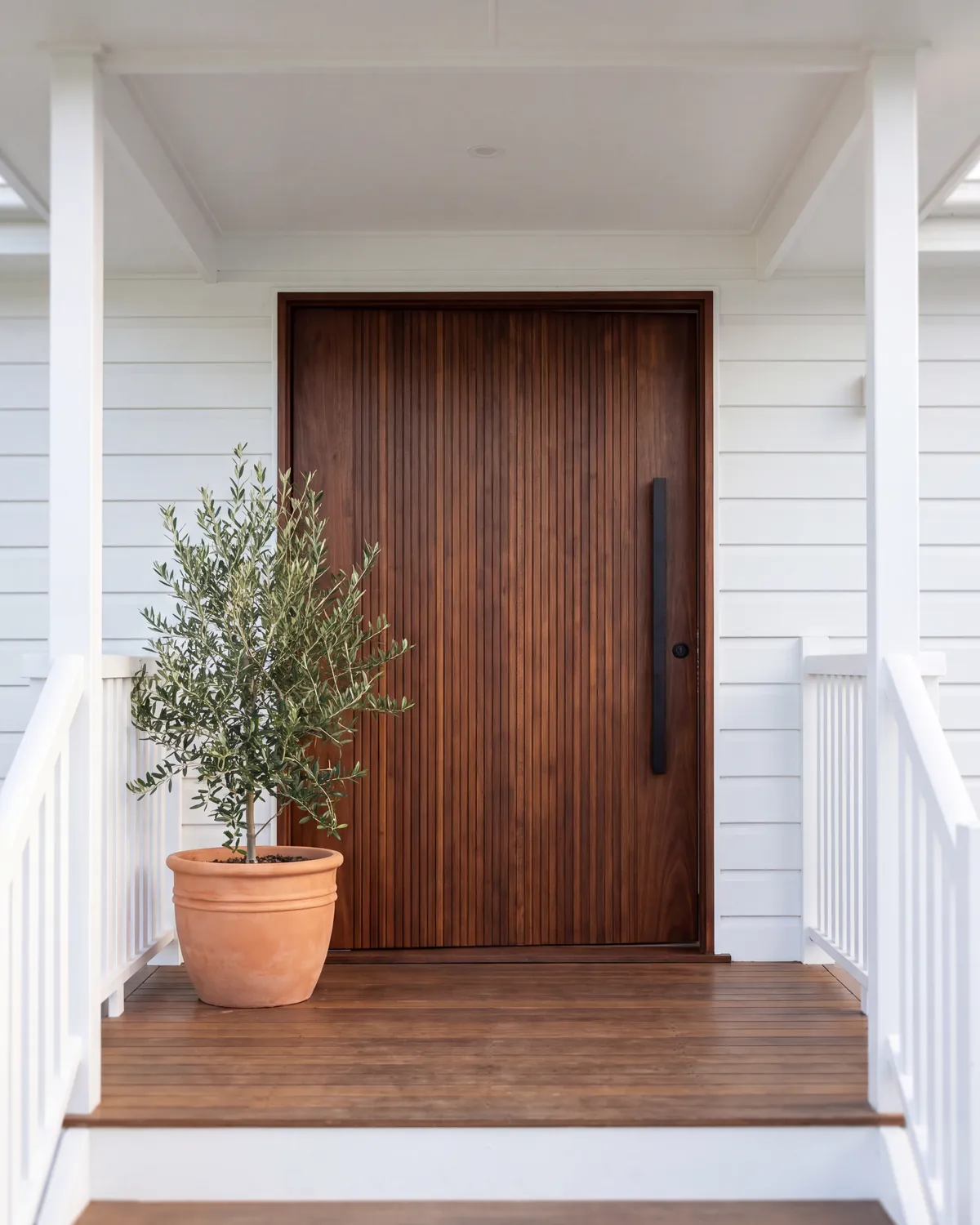 Custom spotted-gum pivot front door with a tall black pull handle on a white weatherboard home